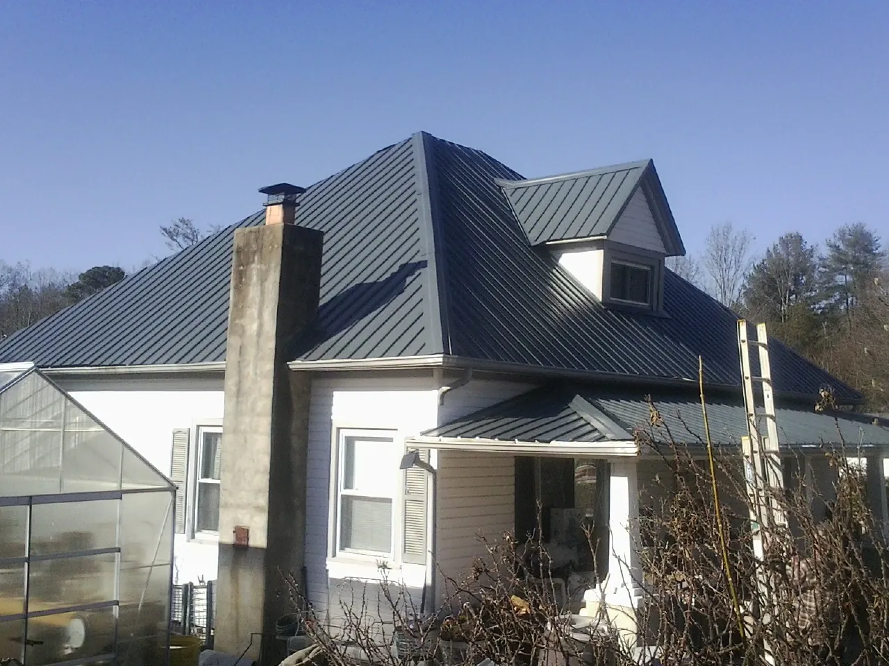 Dark blue standing seam metal roof on a white farmhouse with dormer — Slate & Tile Roof Repair by Roofing Brothers in Le Roy