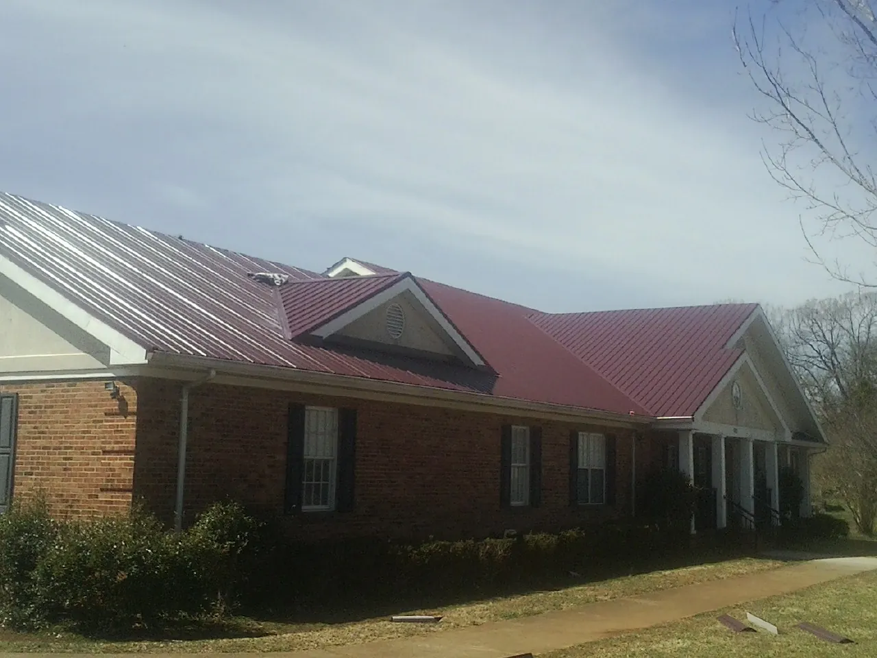 Red metal roof with gabled entries on a long brick building, from a Hail Damage Roof Repair job in Le Roy