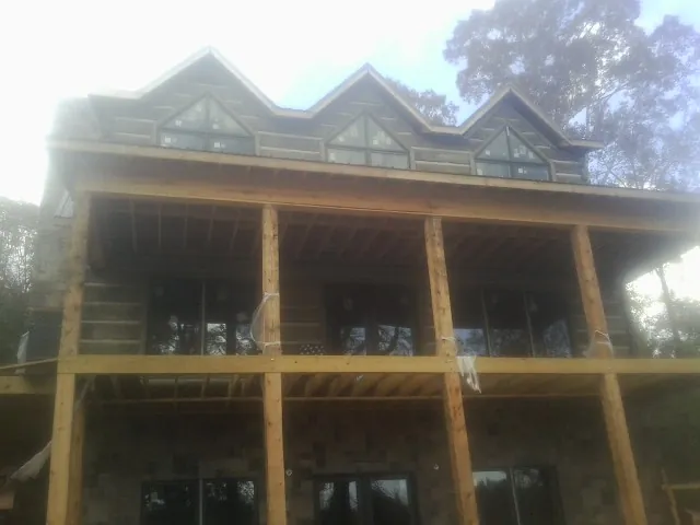 Dormers and porch framing on a large log home under construction — Roof Coating work by our crew in Le Roy