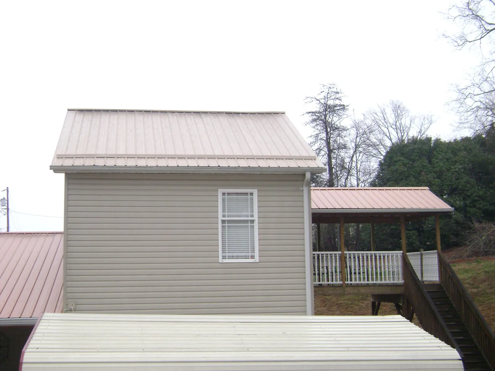 Tan metal roofs on a two story addition and attached porch, from a Roof Replacement job in Le Roy
