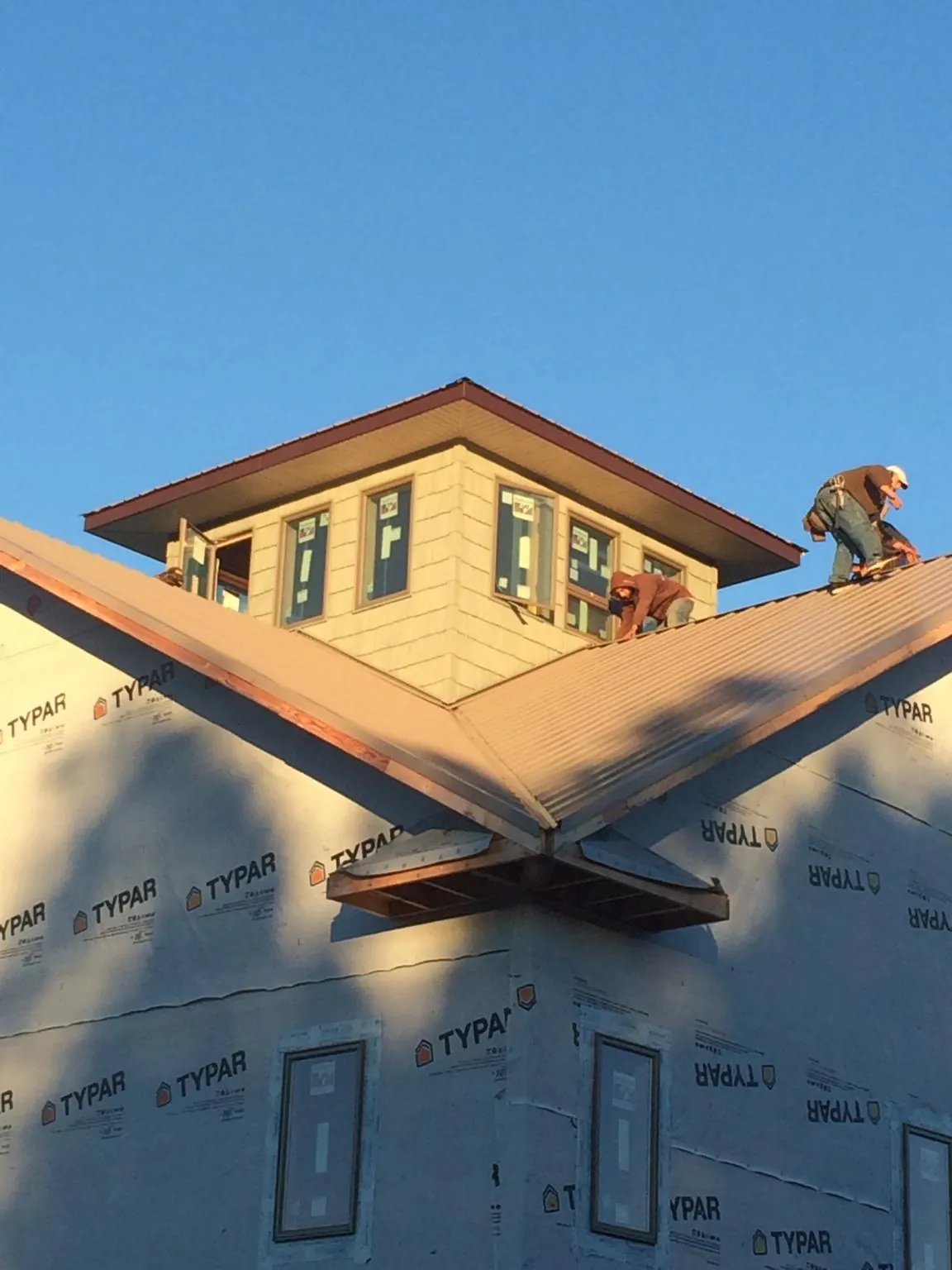Roofers working around a rooftop cupola on a new metal roof at sunset — Roof Waterproofing in Le Roy by Roofing Brothers